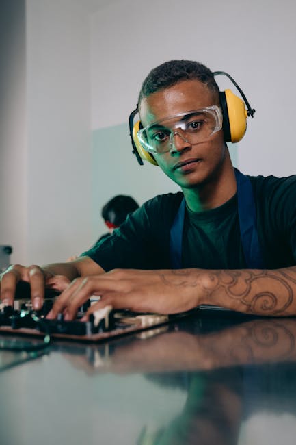 Focused young engineer wearing safety gear repairing electronic equipment indoors.